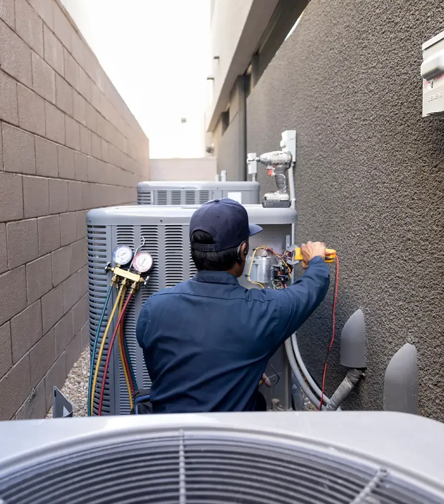 An Anytime technician working on an outdoor AC condenser in a side yard