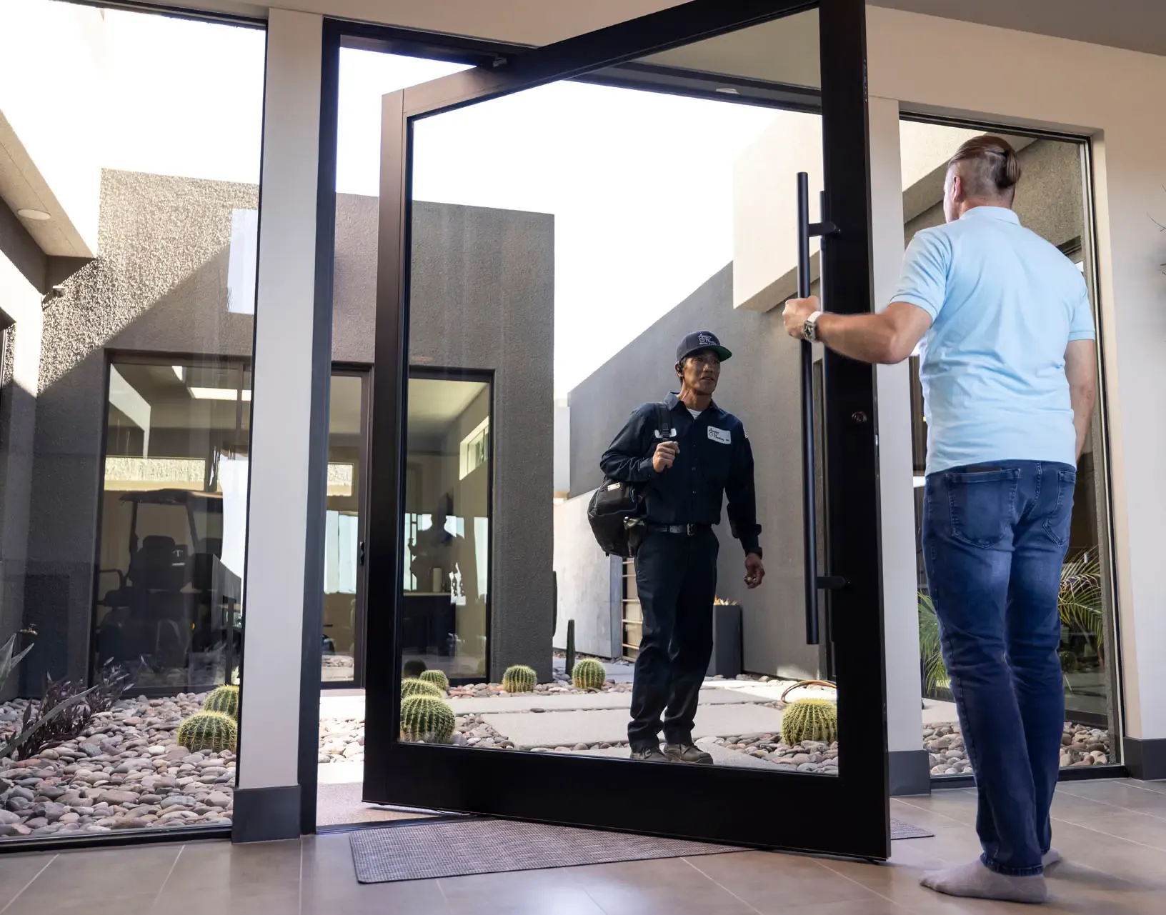 An Anytime technician arriving at a tall pivot front door as a man opens it