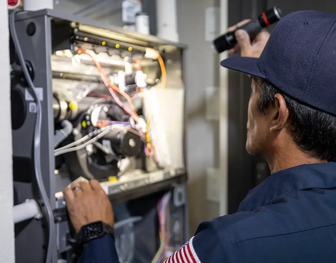 An Anytime technician shining a flashlight into an open furnace cabinet