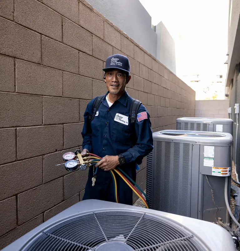 An Anytime technician holding refrigerant gauge hoses beside outdoor AC condensers