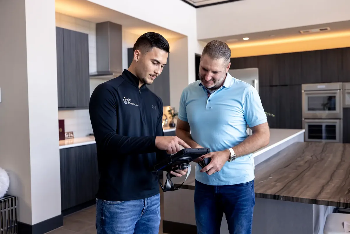 An Anytime technician showing a tablet to a man in a light-blue shirt in a modern kitchen