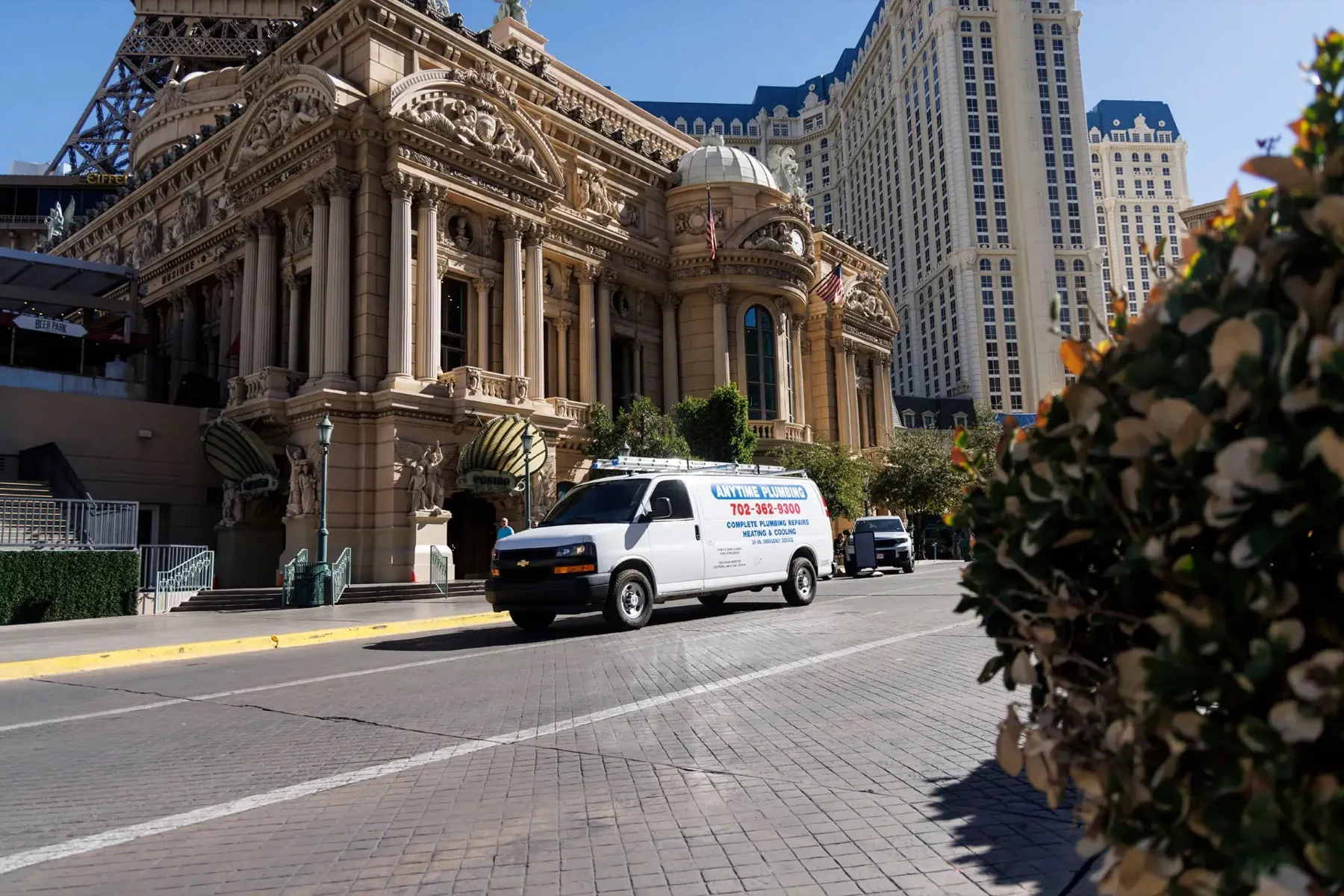 A white Anytime Plumbing van driving past an ornate casino facade on the Las Vegas Strip on a clear day