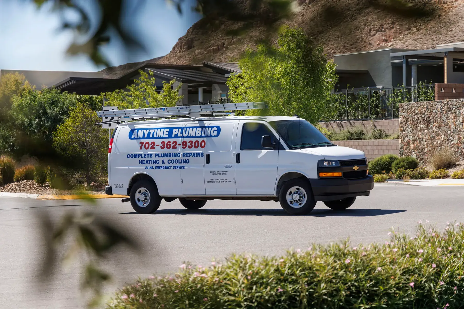 A lettered Anytime Plumbing van parked on a desert neighborhood street below a mountain