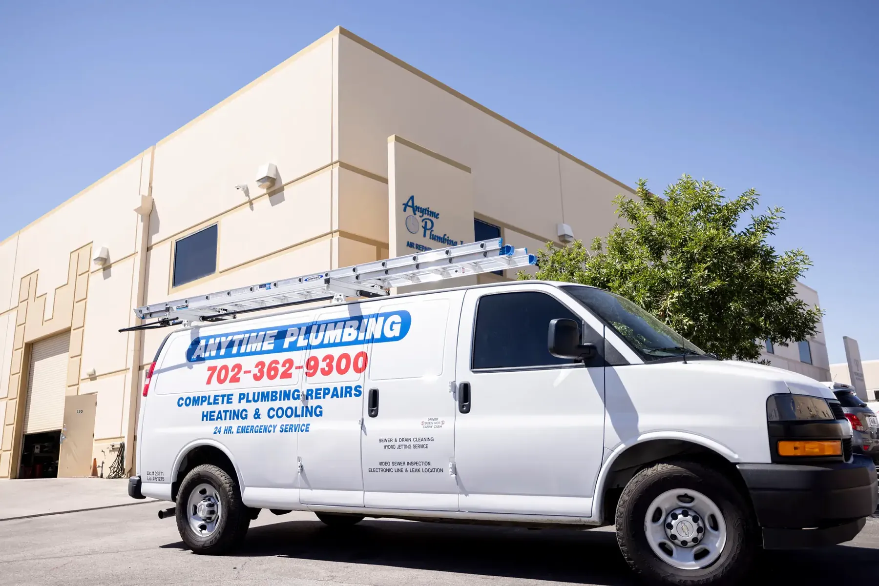A lettered Anytime Plumbing van parked outside a commercial building under a clear sky